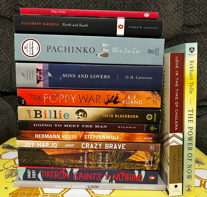 Stack of fourteen books for Adam's 2023 TBR Pile Challenge, twelve stacked vertically with two alternates on the side. 